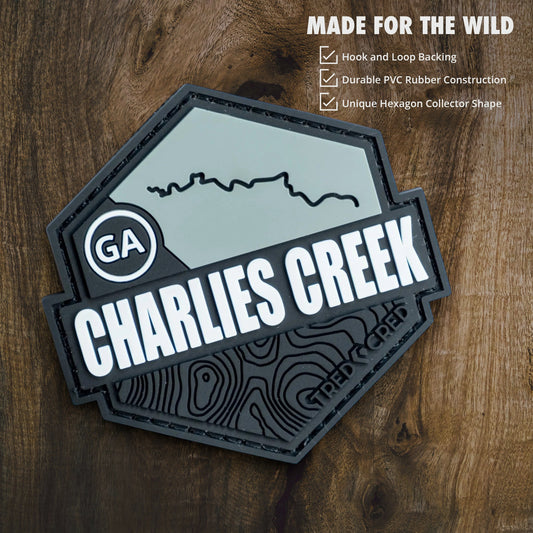 Tred Cred Charlies Creek hexagon PVC trail patch with hook and loop backing on a wooden background