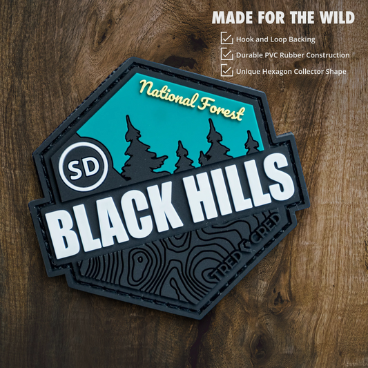 Tred Cred Black Hills National Forest hexagonal PVC patch with teal and black topographic design on wood background.