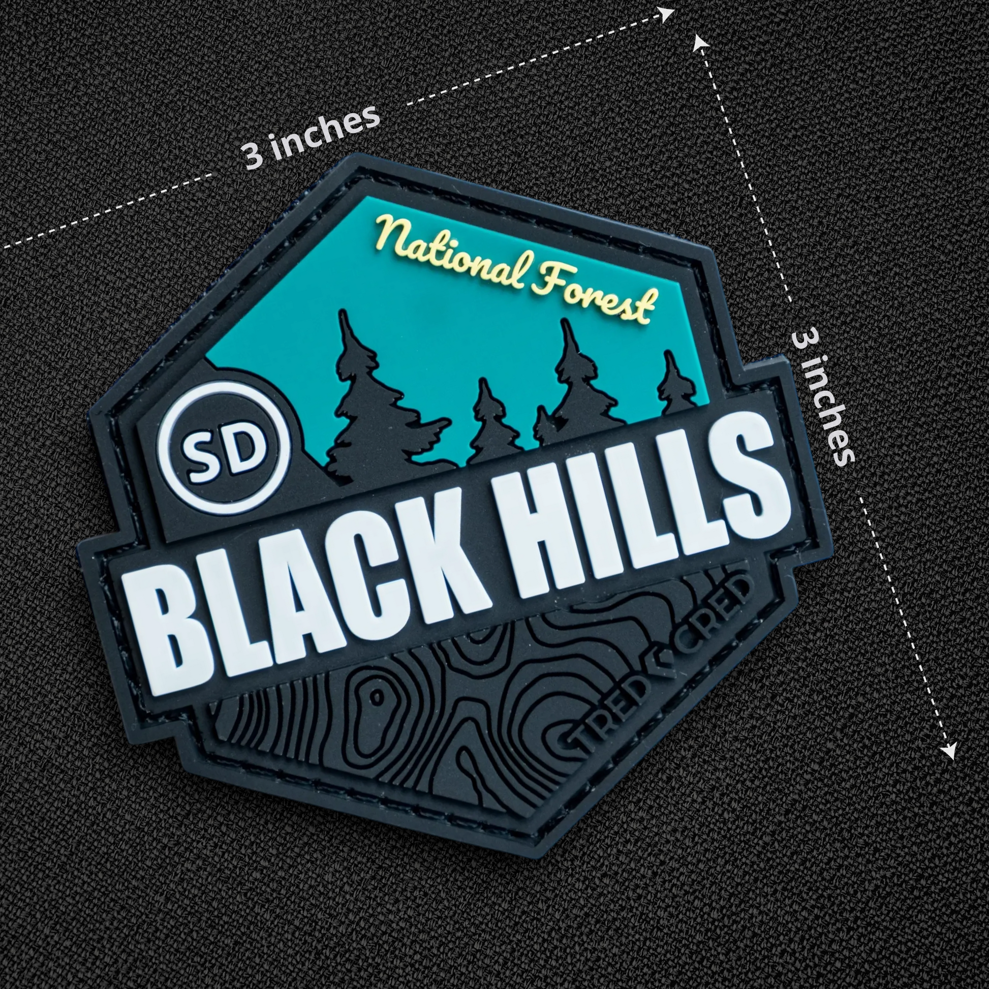 Tred Cred Black Hills National Forest PVC patch with teal and black topographic design and hook and loop backing.