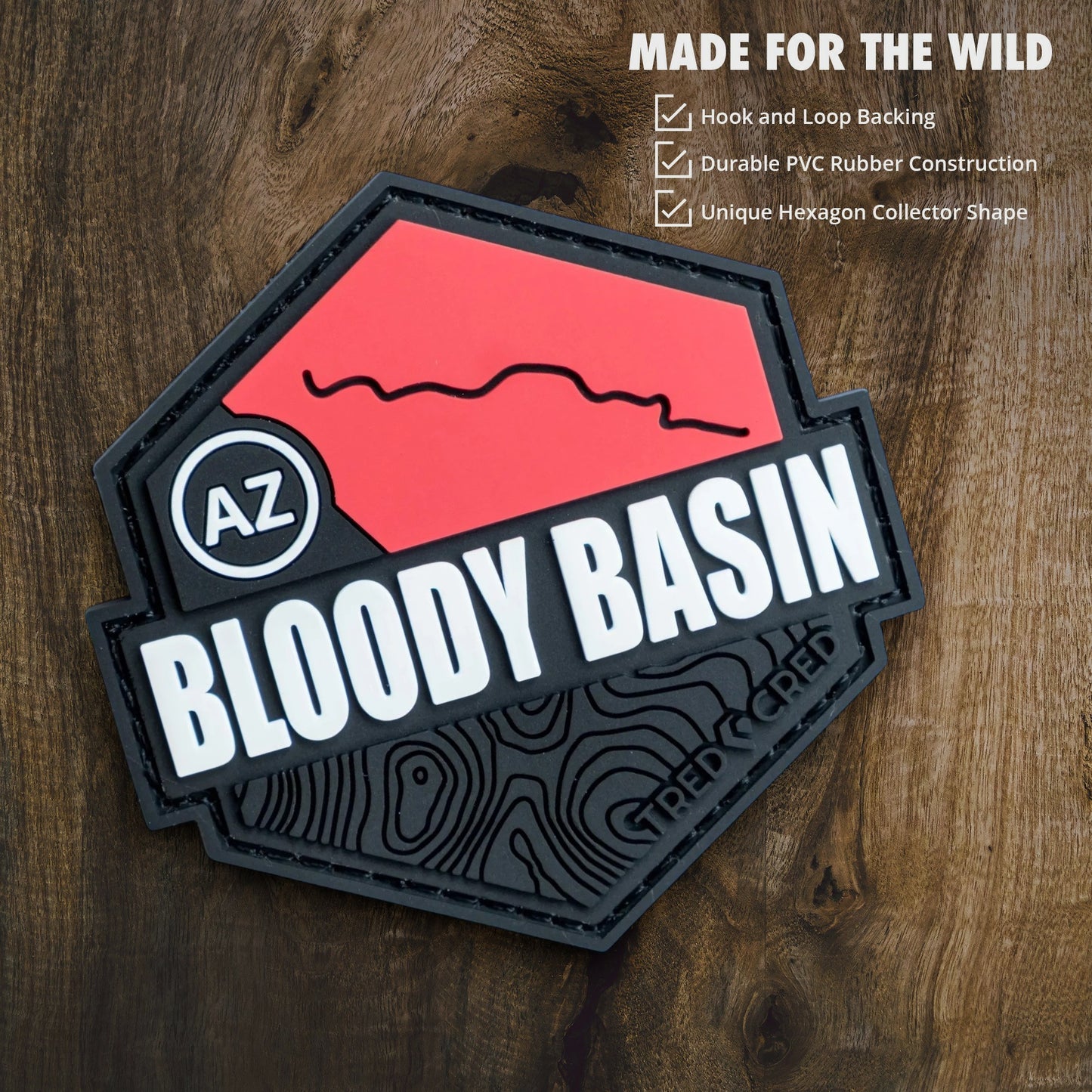 Tred Cred Bloody Basin hexagon PVC trail patch with red and black design and hook and loop backing on wood surface