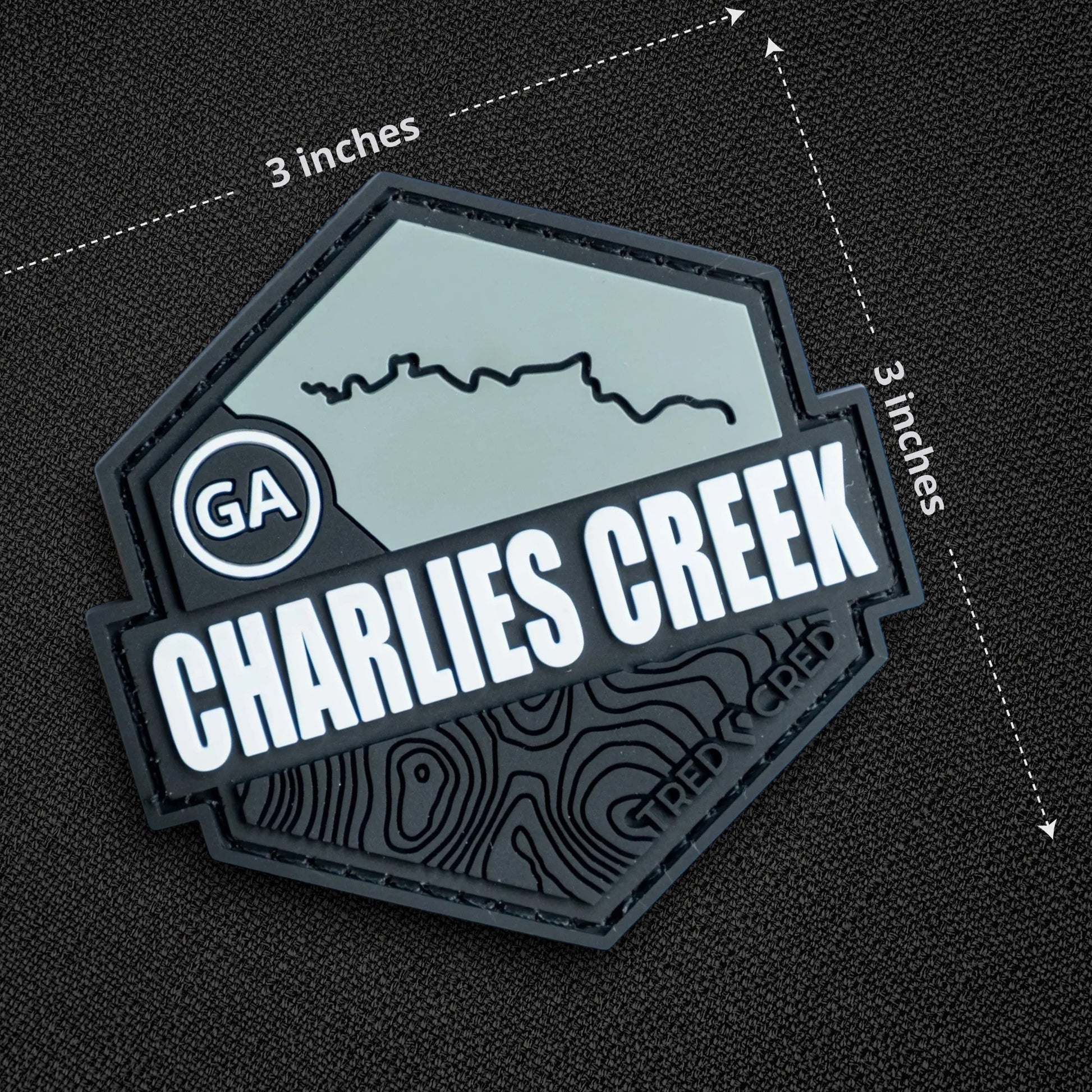 Tred Cred Charlies Creek PVC trail patch with topographic map design and hook and loop backing on black fabric.