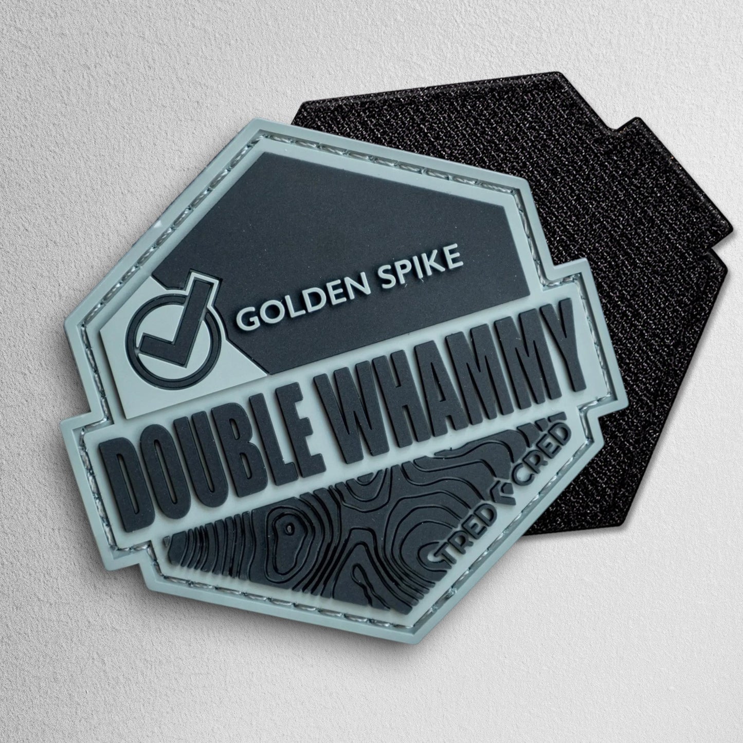 Tred Cred Double Whammy hexagonal PVC trail patch in grey and black with topographic map detail and hook backing