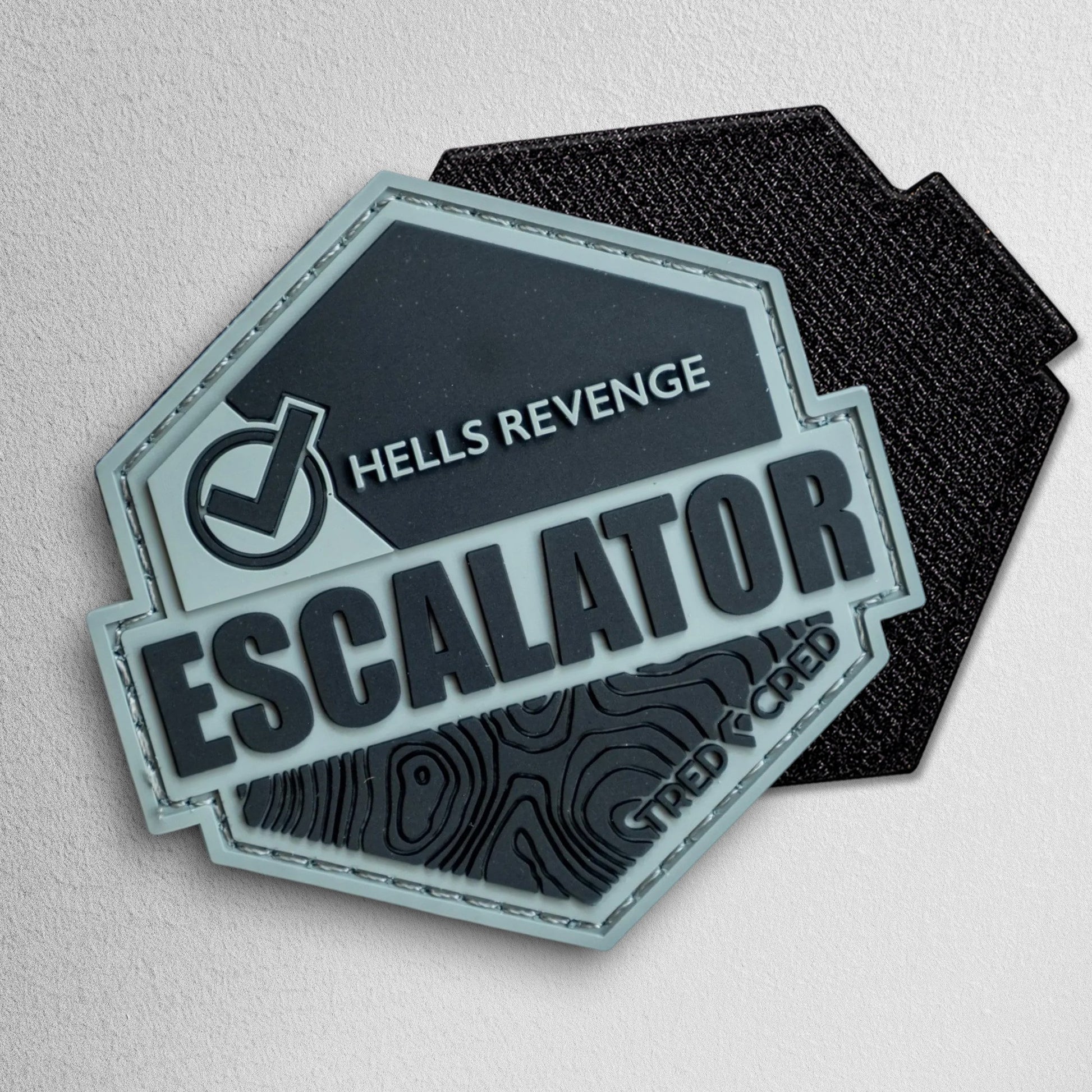 Tred Cred Escalator PVC trail patch with Hells Revenge text and topographic map design in grey and black
