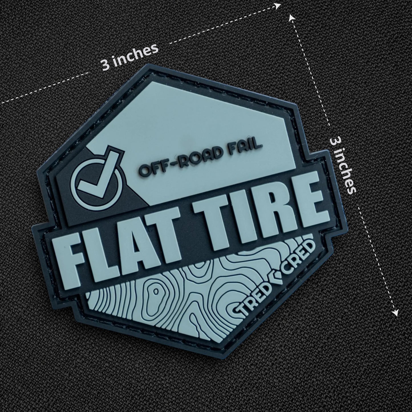 Tred Cred Flat Tire PVC patch with off-road topography design and hook and loop backing on a grey background.