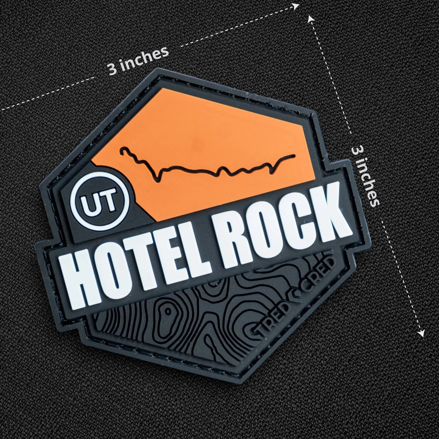 Tred Cred Hotel Rock PVC trail patch with orange and black topographic design and hook and loop backing.