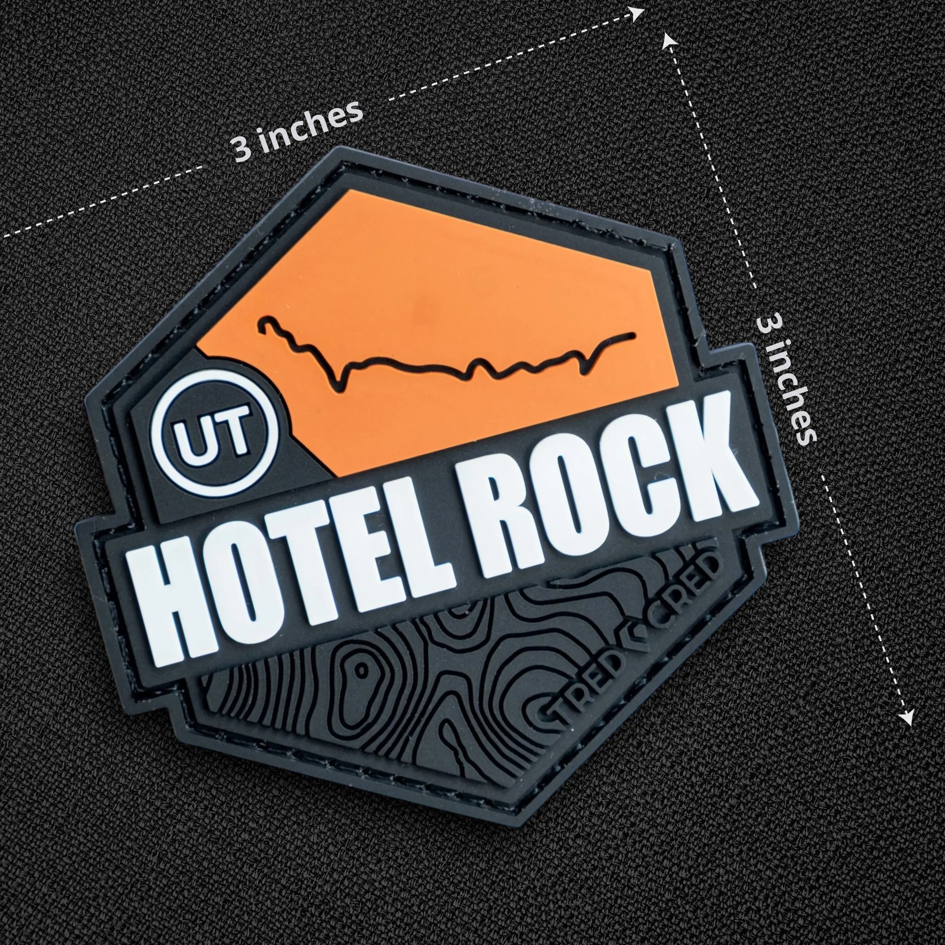 Tred Cred Hotel Rock PVC trail patch with orange and black topographic design and hook and loop backing.
