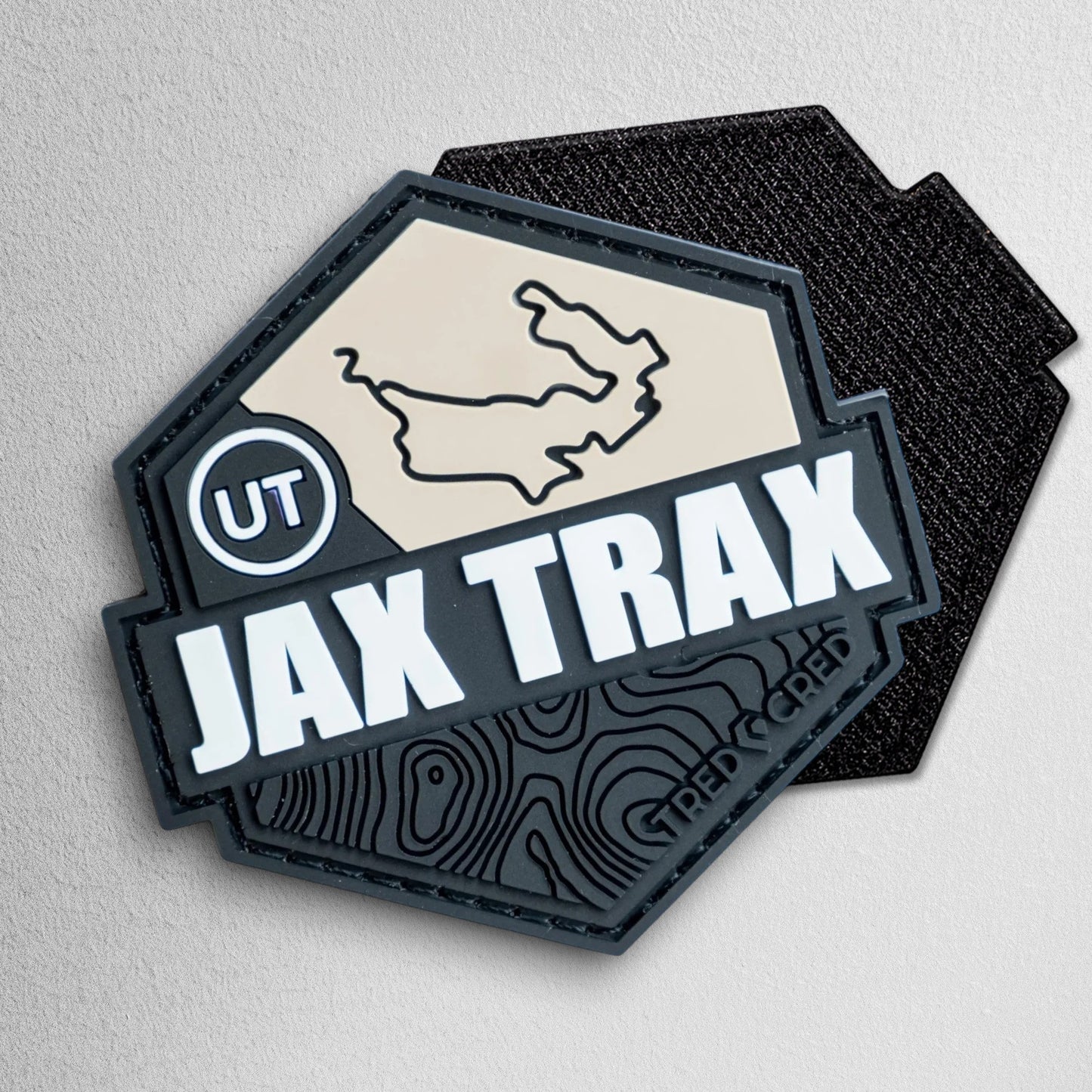 Tred Cred Jax Trax hexagonal PVC rubber trail patch with a tan map, white text, and black topographical design.