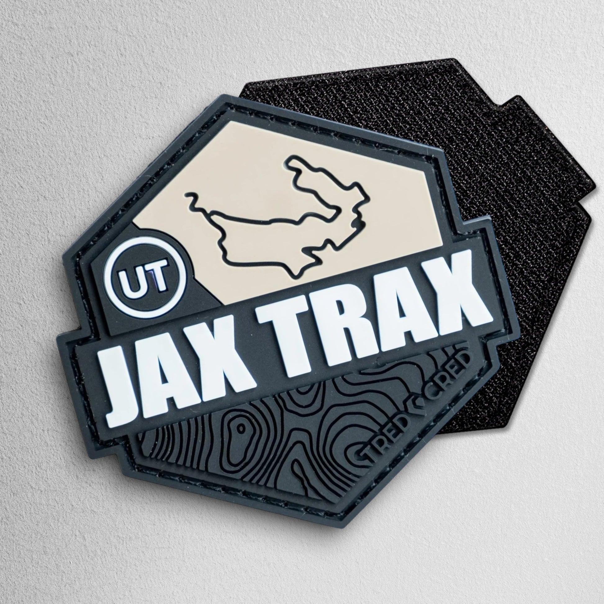 Tred Cred Jax Trax hexagonal PVC rubber trail patch with a tan map, white text, and black topographical design.