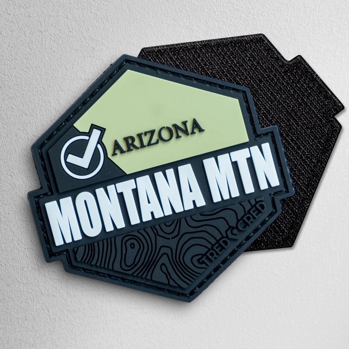 Tred Cred Montana Mountain hexagonal PVC patch with green and black topographic design and hook and loop backing.