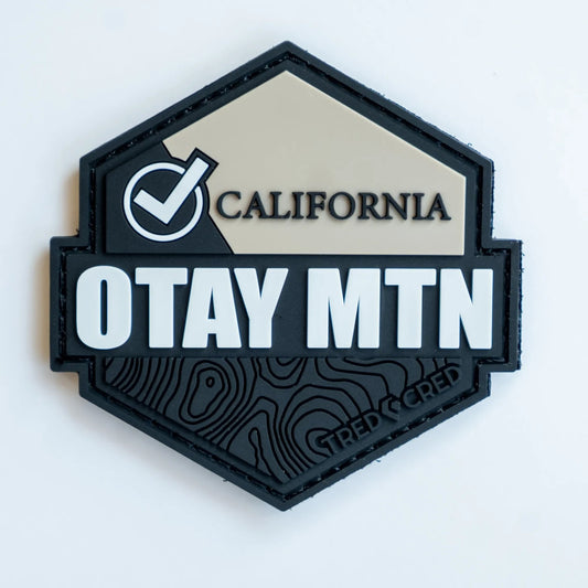 Tred Cred Otay Mountain hexagonal PVC patch in black and tan with topographic map details and hook and loop backing.