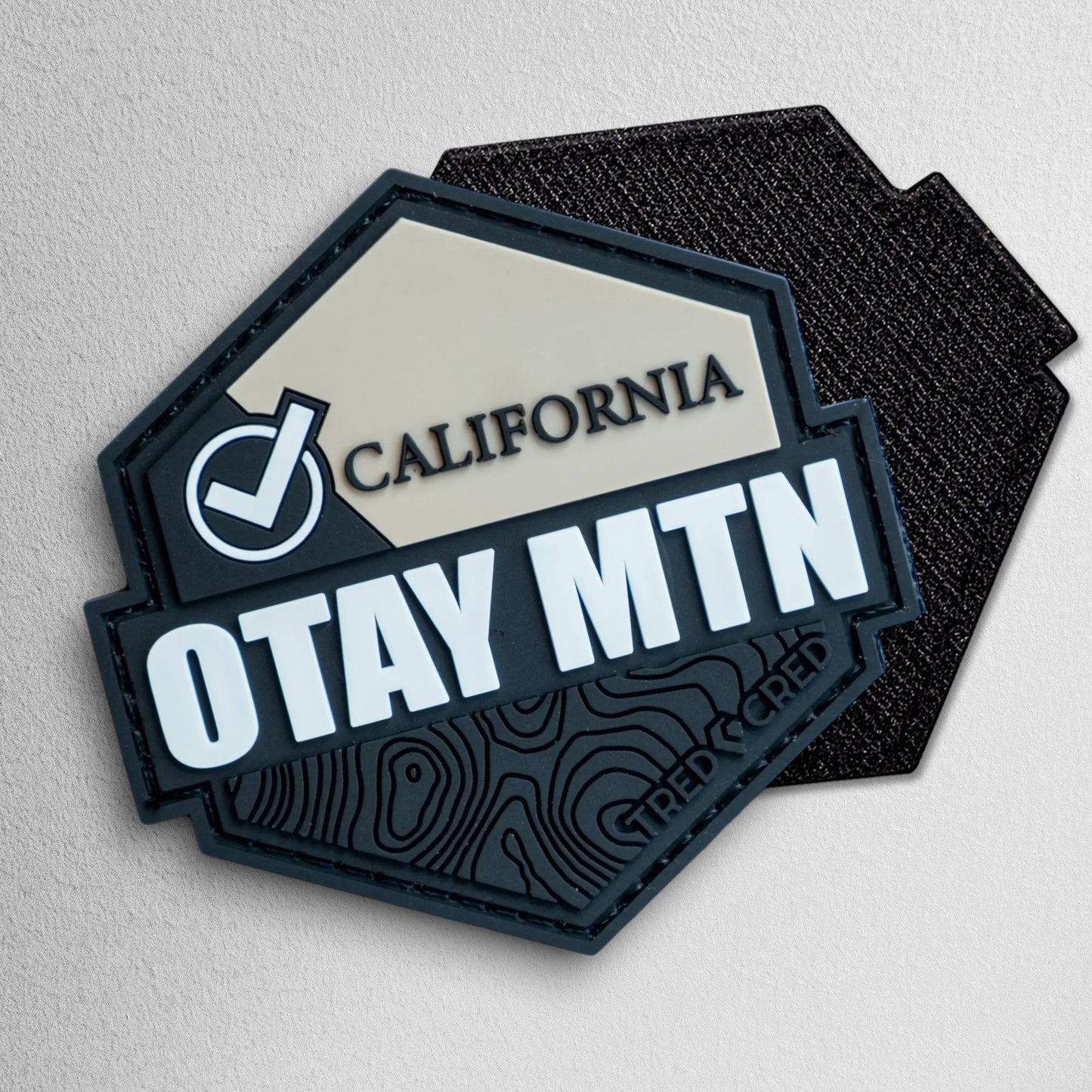 Tred Cred Otay Mountain PVC trail patch with topographic map design, checkmark icon, and hook and loop backing.