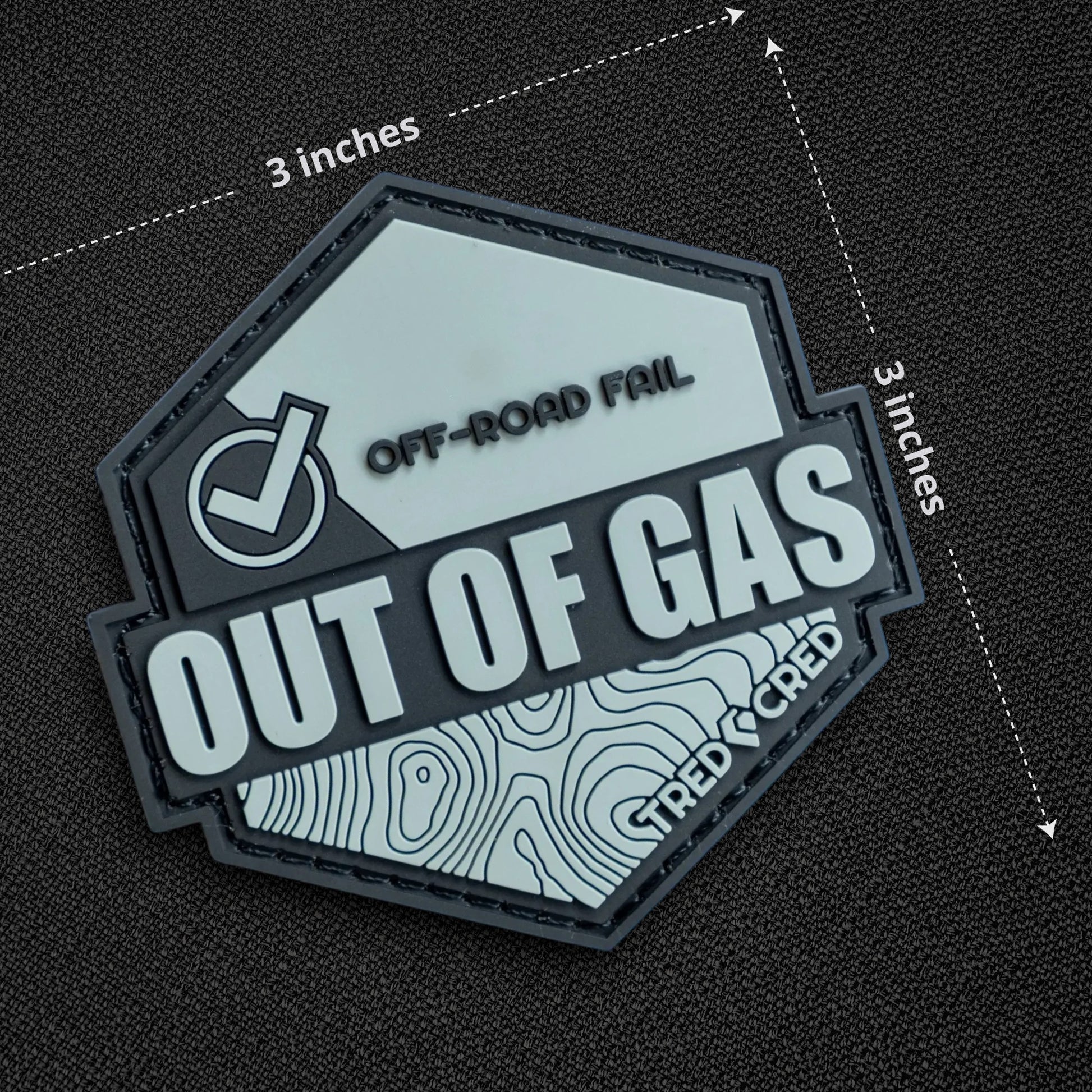 Tred Cred Out of Gas hexagonal PVC patch with topographic map design and hook and loop backing on wood background.