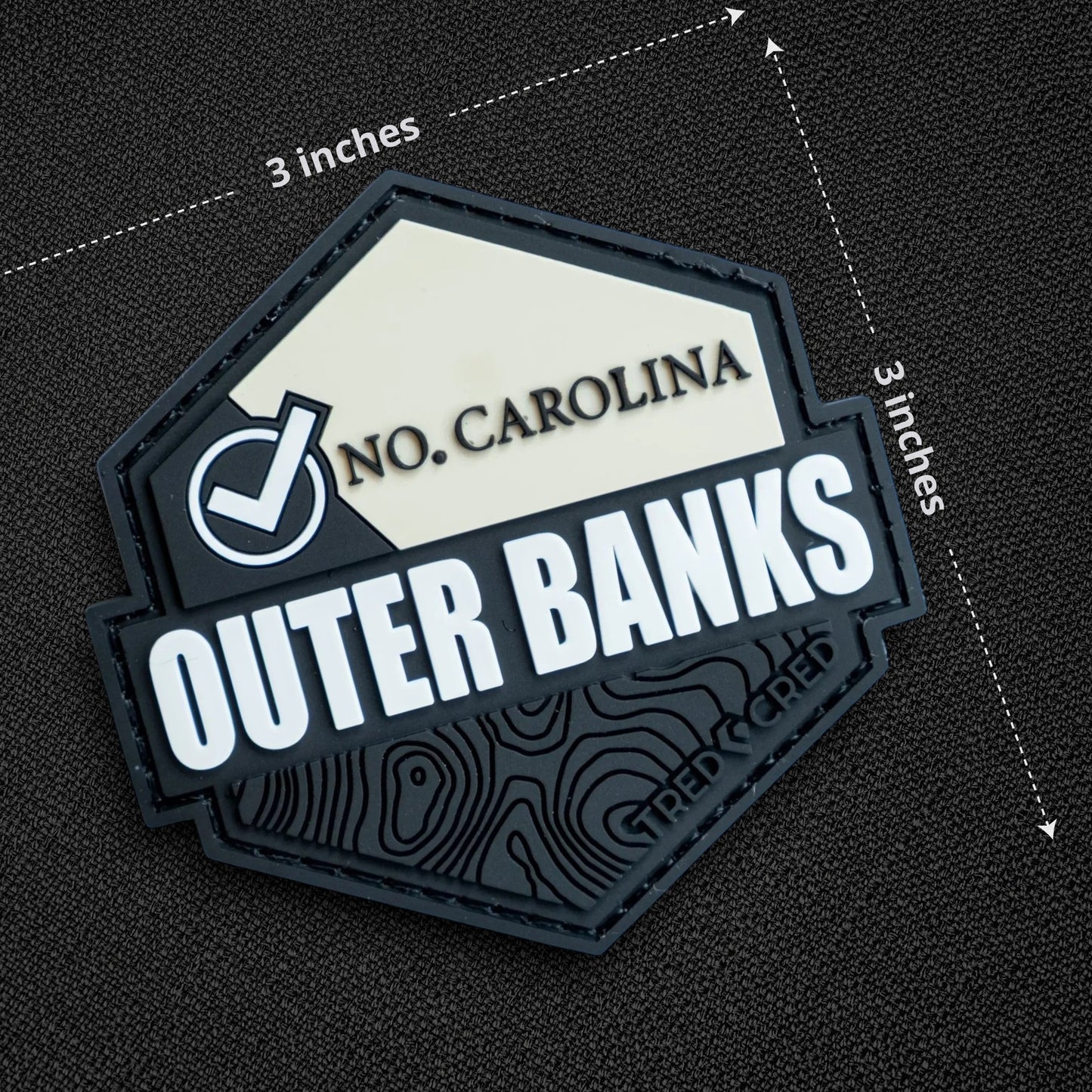 Tred Cred Outer Banks hexagonal PVC patch with North Carolina text and topographic map design on black fabric