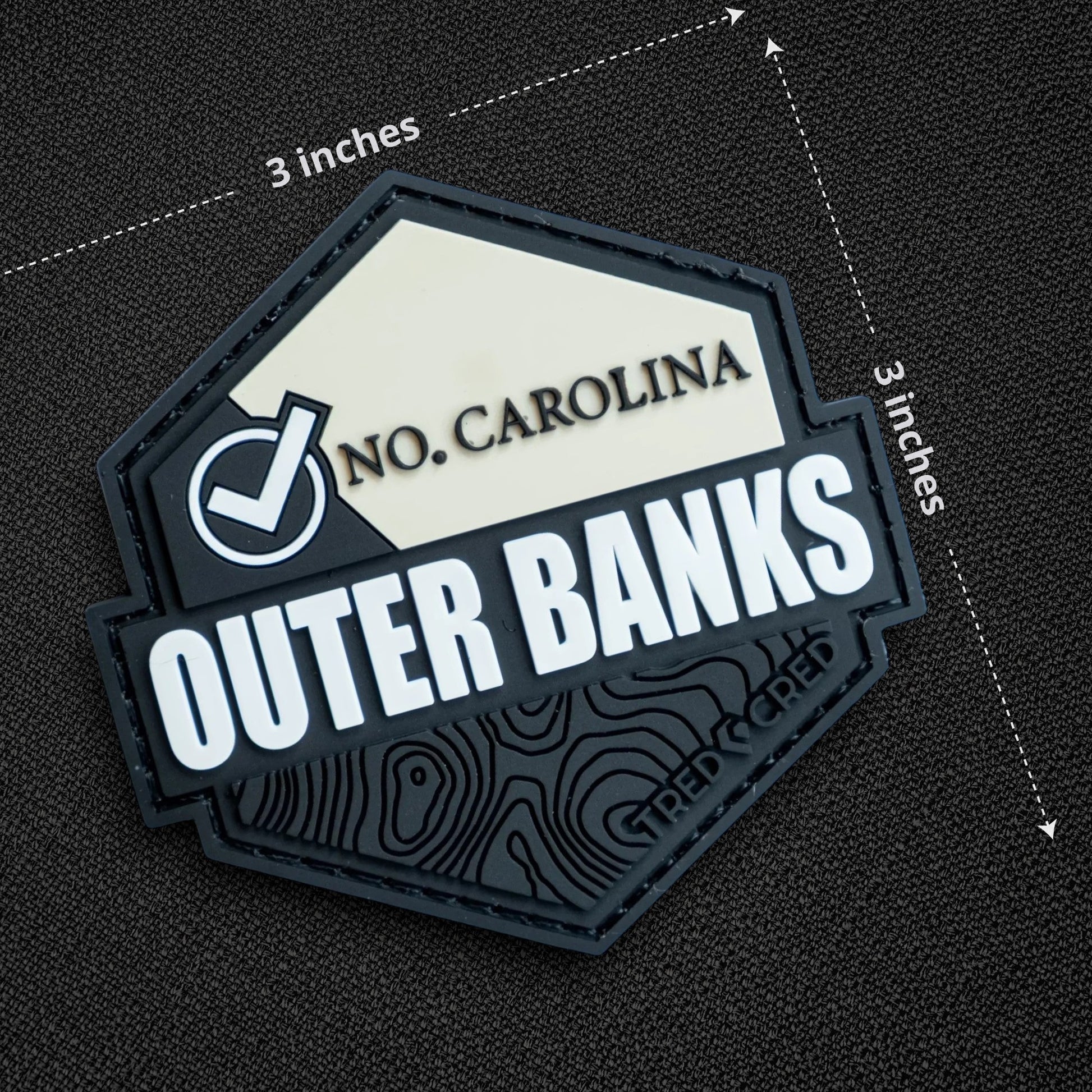 Tred Cred Outer Banks hexagonal PVC patch with North Carolina text and topographic map design on black fabric