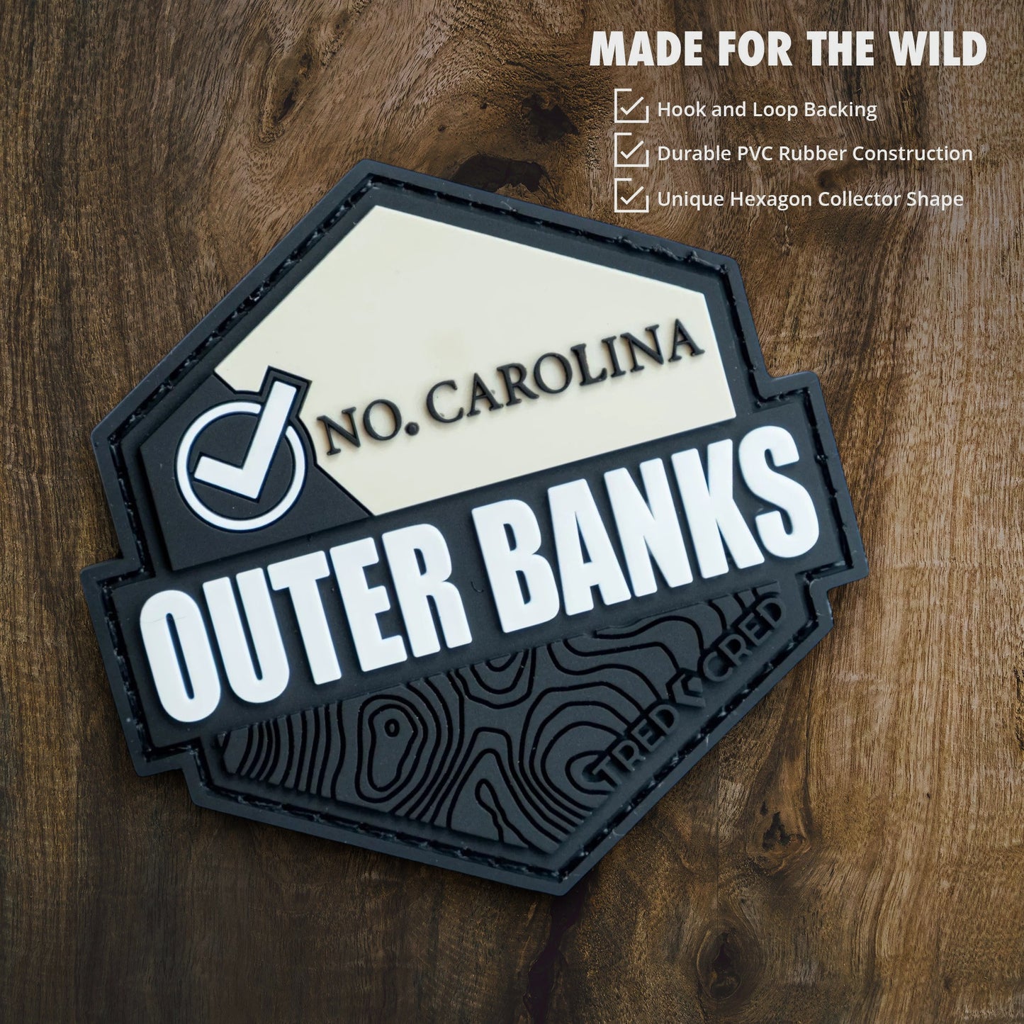 Tred Cred Outer Banks hexagon PVC rubber trail patch with hook and loop backing on a wooden background
