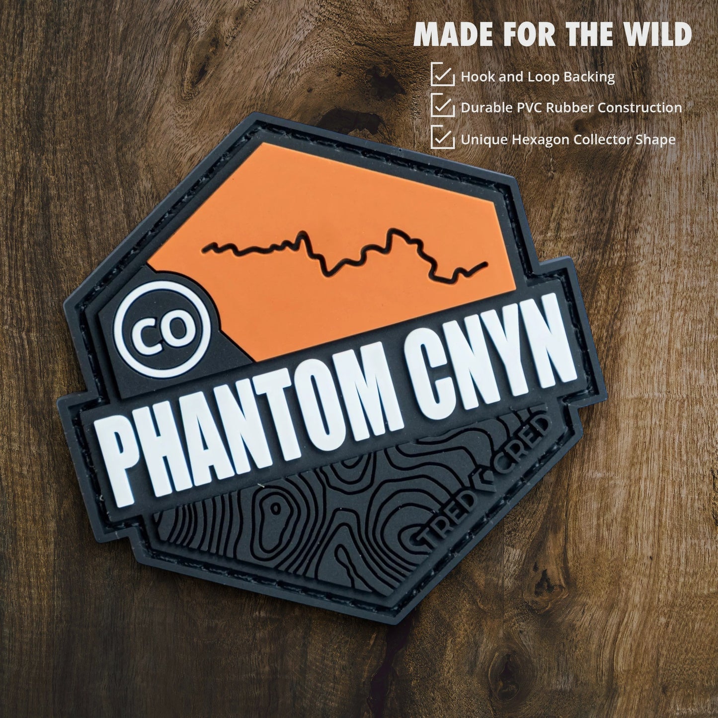Tred Cred Phantom Canyon hexagon PVC rubber trail patch with orange and black topographic design on wood background