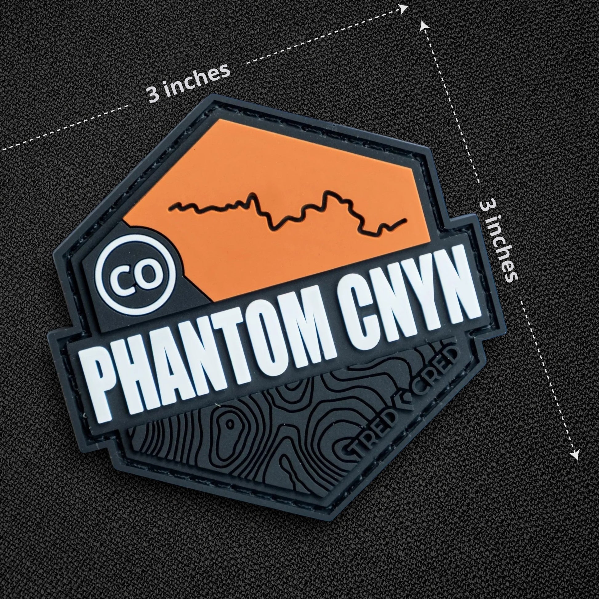 Tred Cred Phantom Canyon PVC trail patch with orange and black topographic design and hook and loop backing.