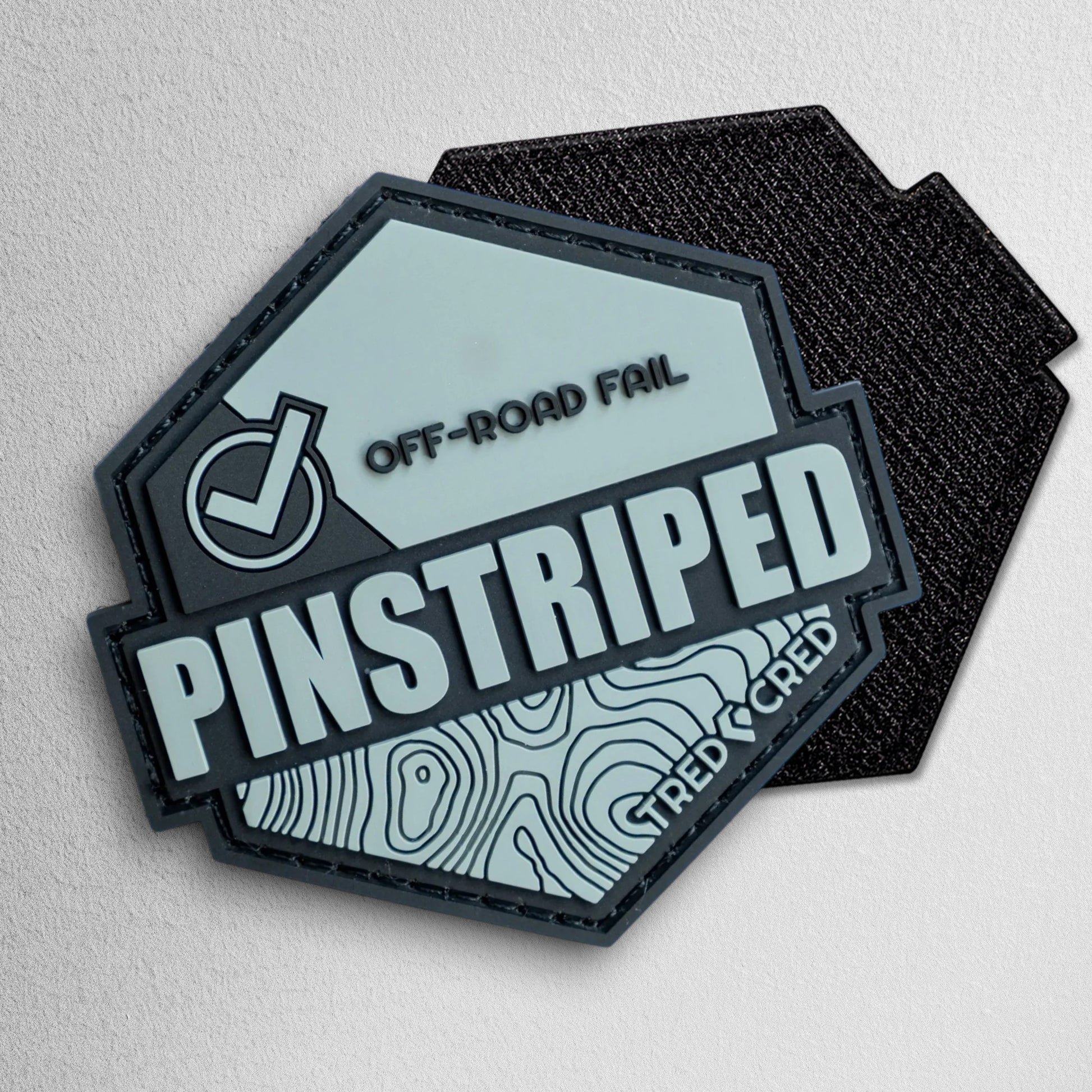 Tred Cred Pinstriped hexagonal PVC patch in grey and black with off-road fail text and topographical map design.