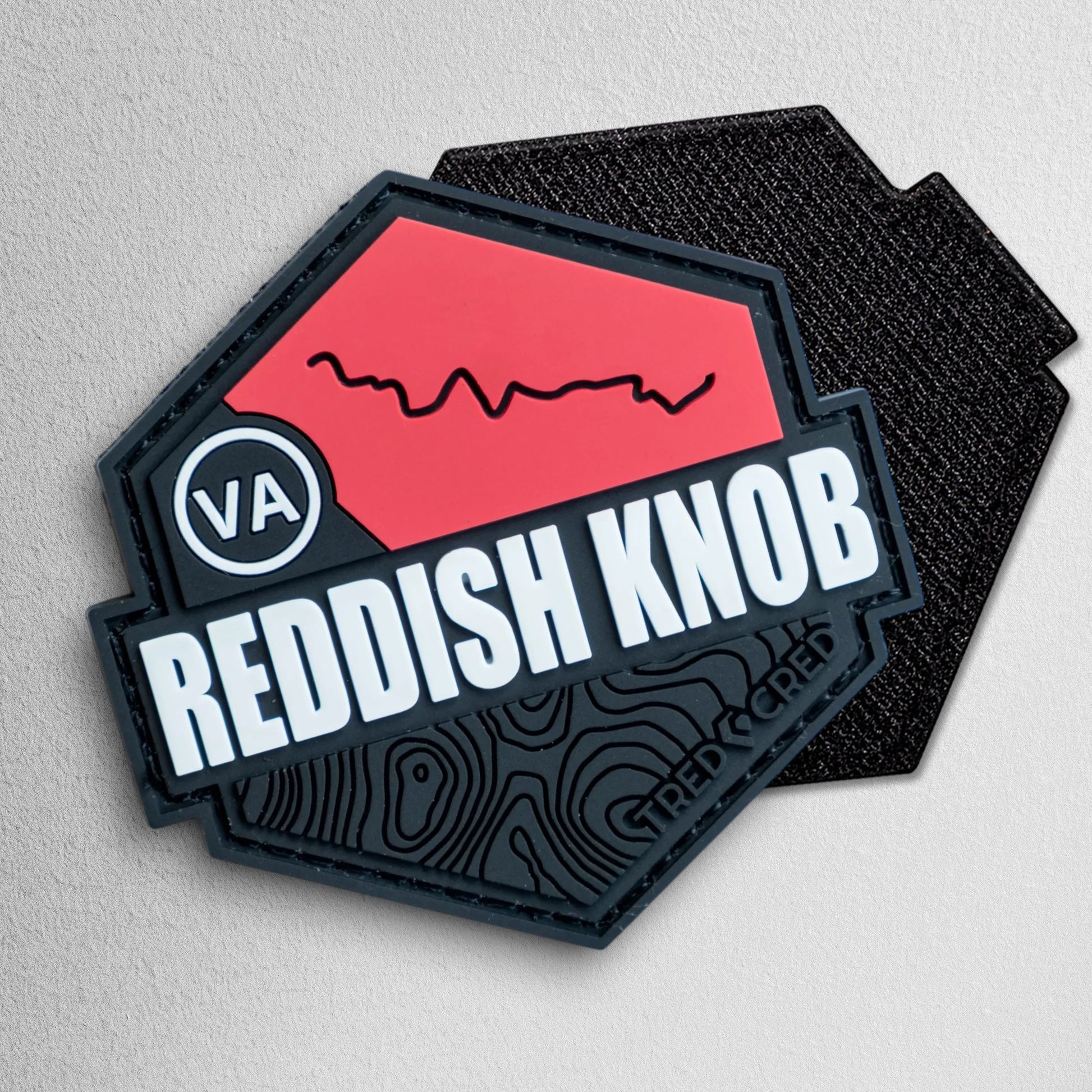 Tred Cred Reddish Knob hexagonal PVC rubber trail patch with red and black topographic design and hook backing.