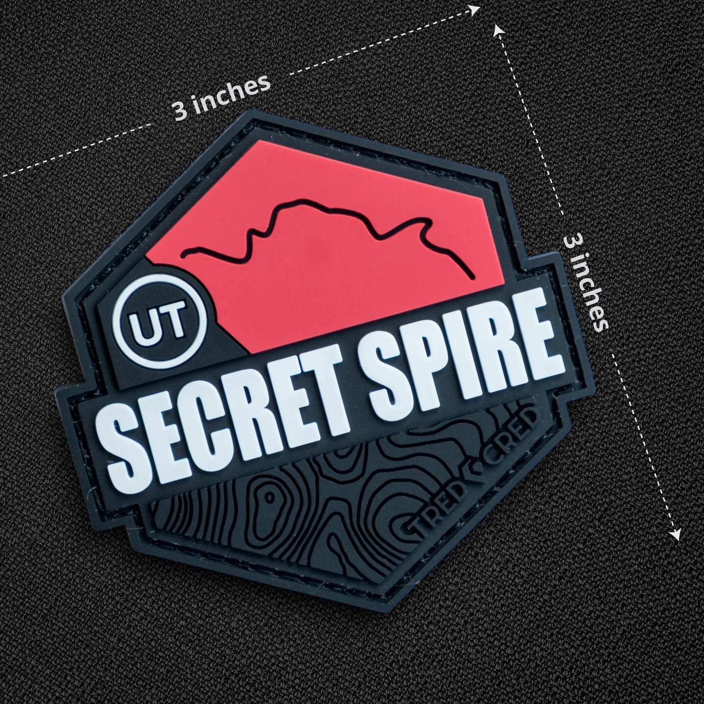 Tred Cred Secret Spire PVC trail patch with red mountain graphic, white text, and black hook and loop backing.