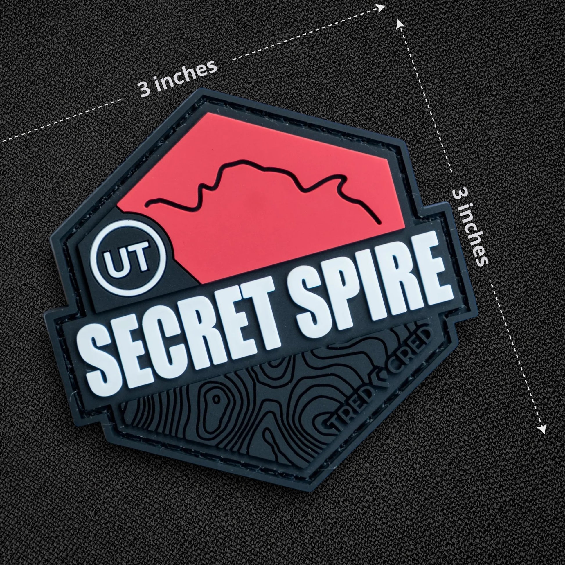 Tred Cred Secret Spire PVC trail patch with red mountain graphic, white text, and black hook and loop backing.
