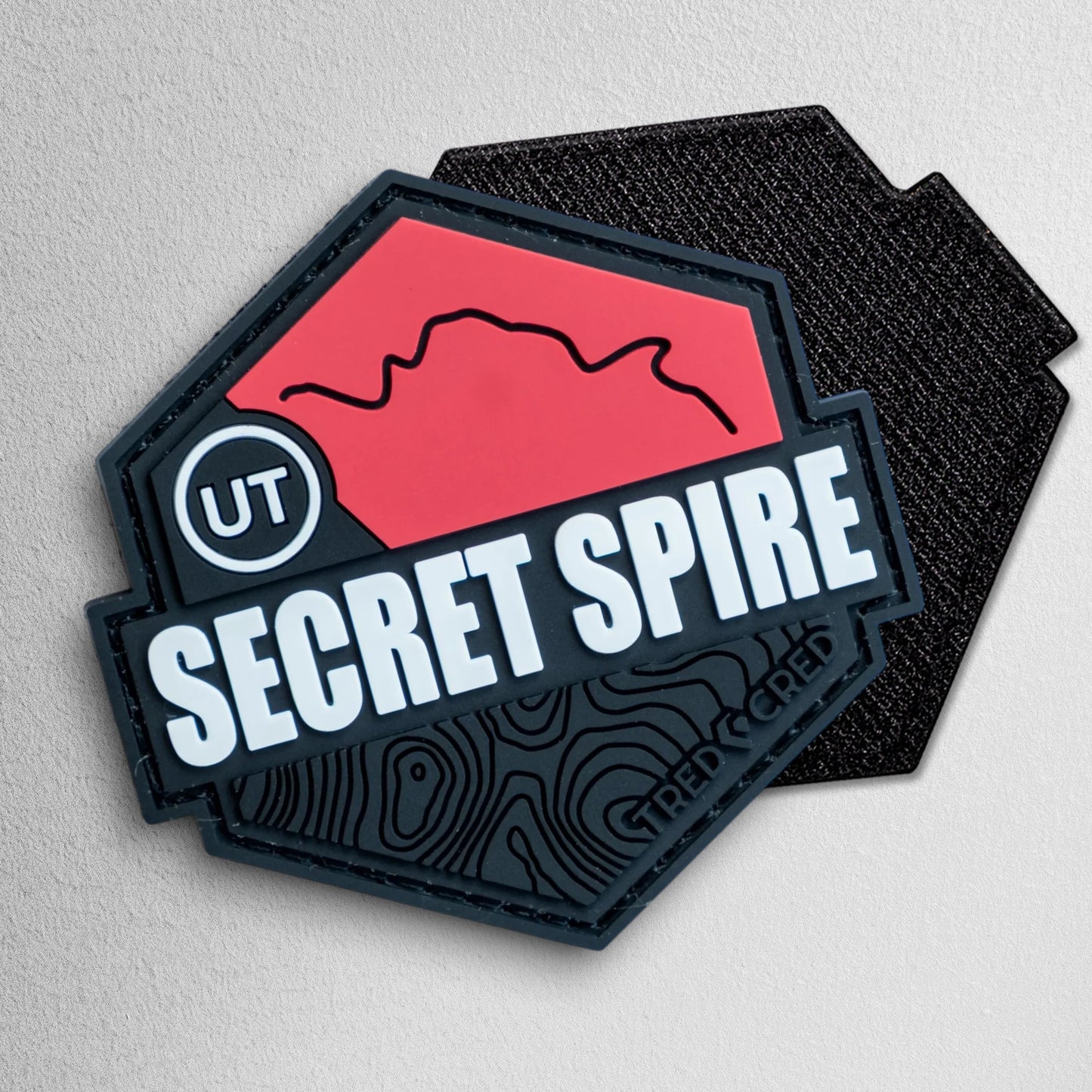 Tred Cred Secret Spire trail patch in red and black PVC rubber with a hexagonal shape and topographic map design.