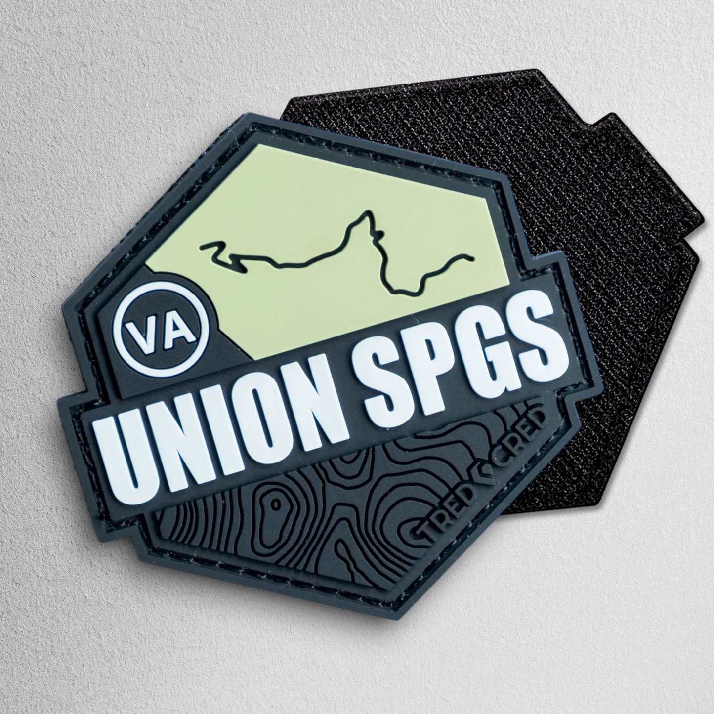 Tred Cred Union Springs hexagonal PVC trail patch in olive green and black with topographic map design.