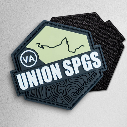 Tred Cred Union Springs hexagonal PVC trail patch in olive green and black with topographic map design.