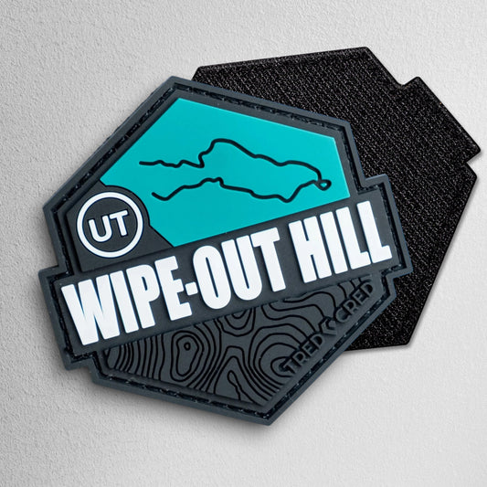 Tred Cred Wipe-Out Hill hexagonal PVC patch in teal and black with topographic map detail and hook and loop backing.