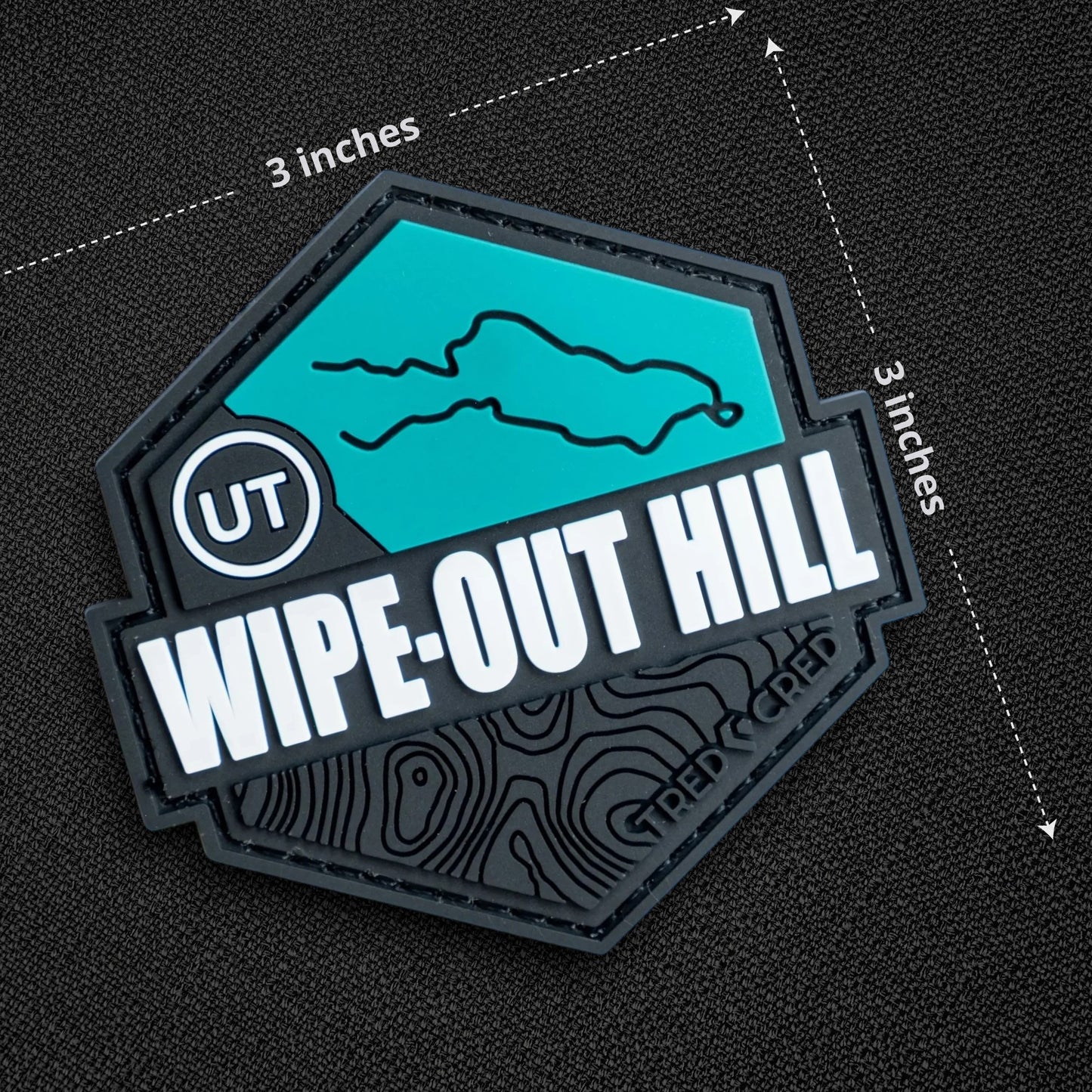 Tred Cred Wipe-Out Hill trail patch in teal and black PVC rubber with hook and loop backing and topographic design.