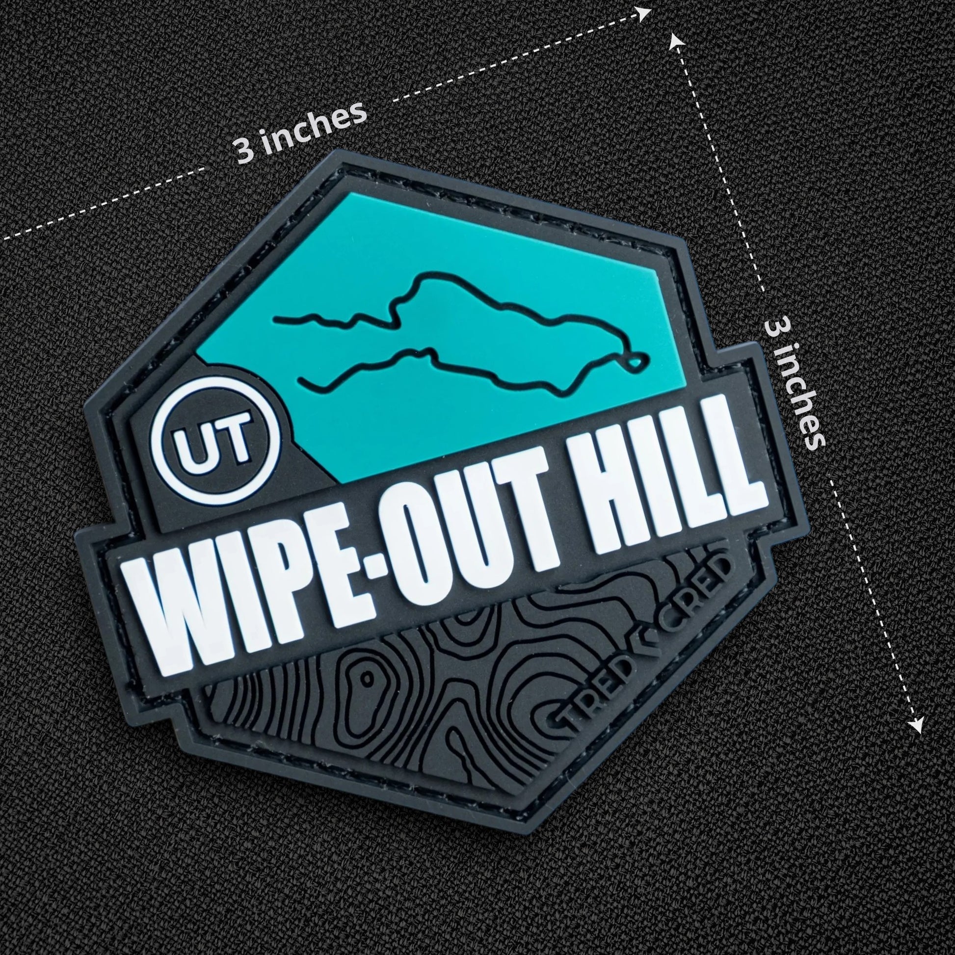 Tred Cred Wipe-Out Hill trail patch in teal and black PVC rubber with hook and loop backing and topographic design.