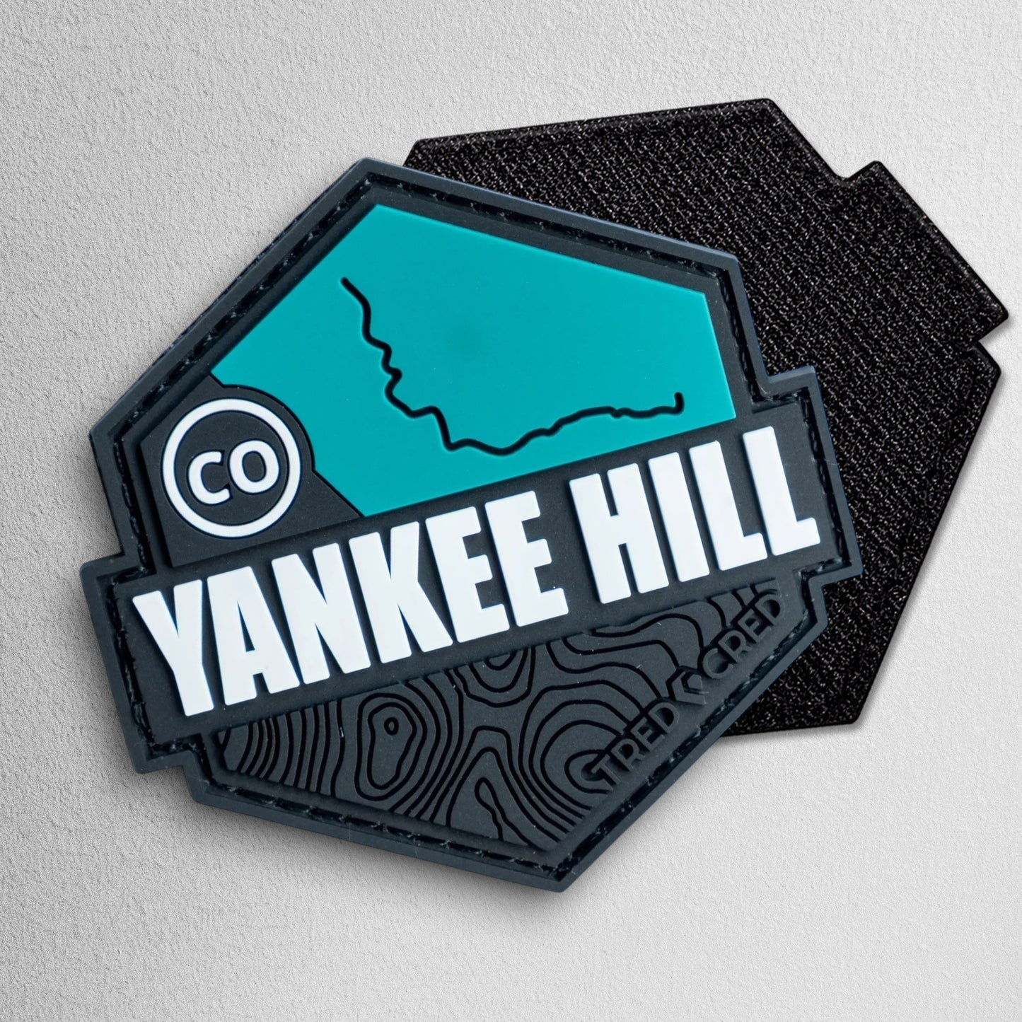 Tred Cred Yankee Hill trail patch in teal and black PVC rubber with topographic map design and hook and loop backing.
