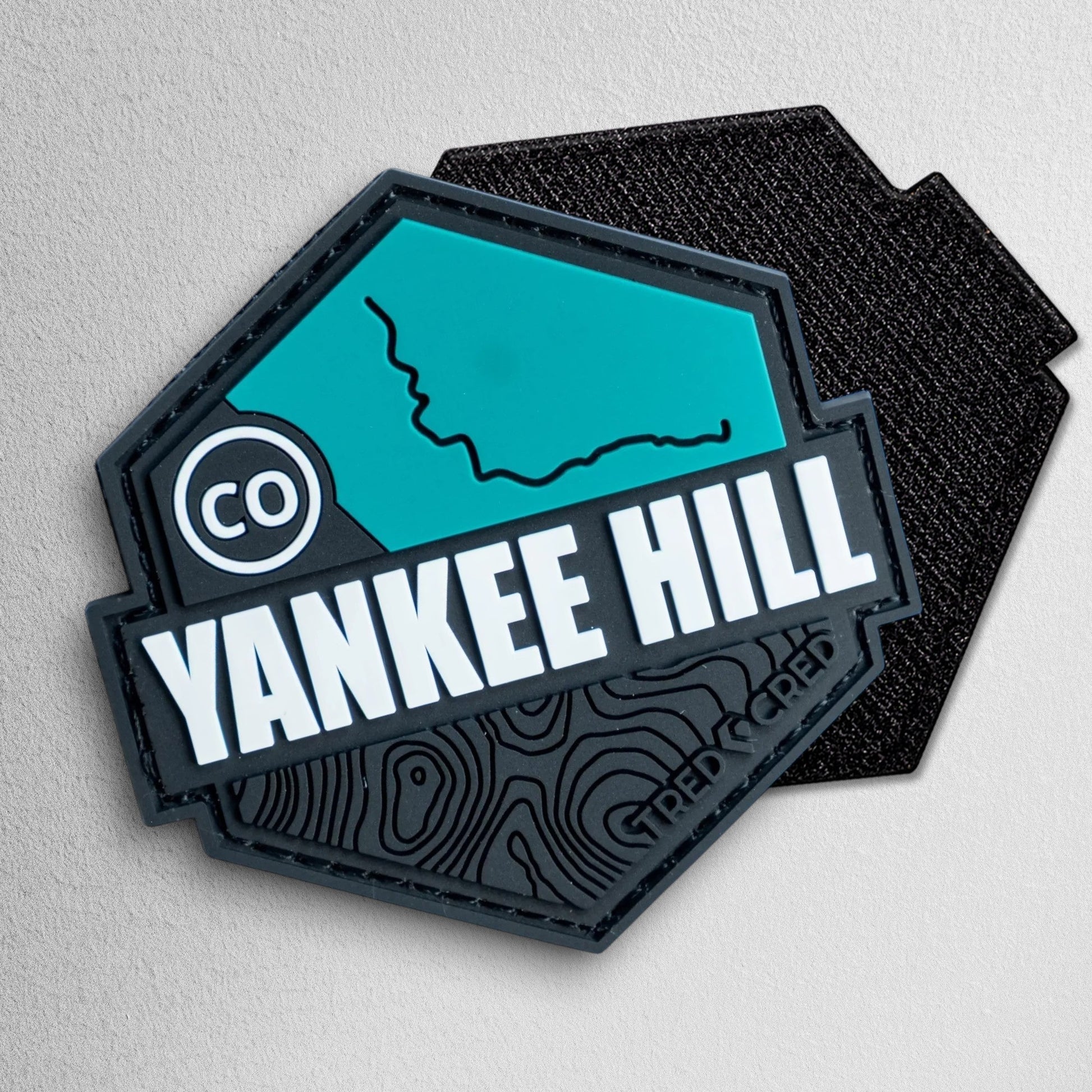 Tred Cred Yankee Hill trail patch in teal and black PVC rubber with topographic map design and hook and loop backing.